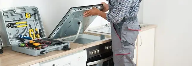 Cooktop repair technician lifting a built-in stovetop for service in Las Vegas, NV