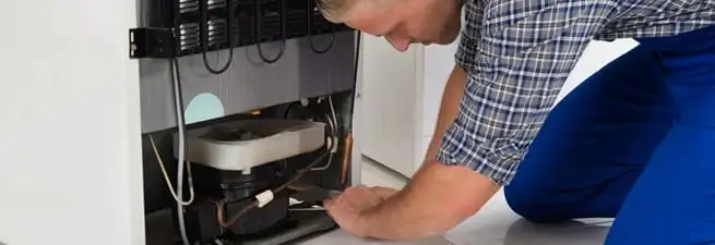 Refrigerator repair technician servicing the compressor and condenser area in Las Vegas, NV