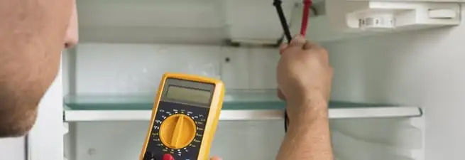 Refrigerator repair technician testing electrical components with a multimeter in Las Vegas, NV